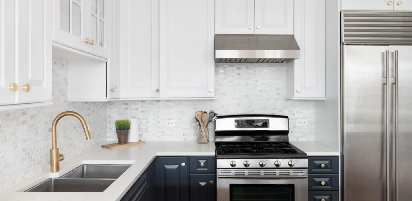 Modern kitchen with white upper cabinets, dark blue lower cabinets, and gold hardware.