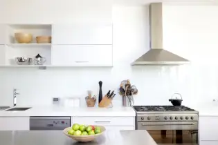 White kitchen with stainless steel appliances and a wall-mount ducted vent hood above a gas range.
