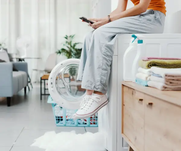 Woman calling a repair service due to a washing machine leaking.