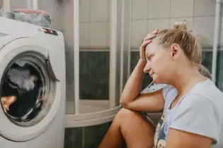 Woman sitting in front of a broken front-load washing machine.