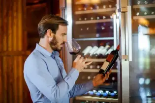 Man drinking red wine out of a glass in front of a built-in wine cooler.